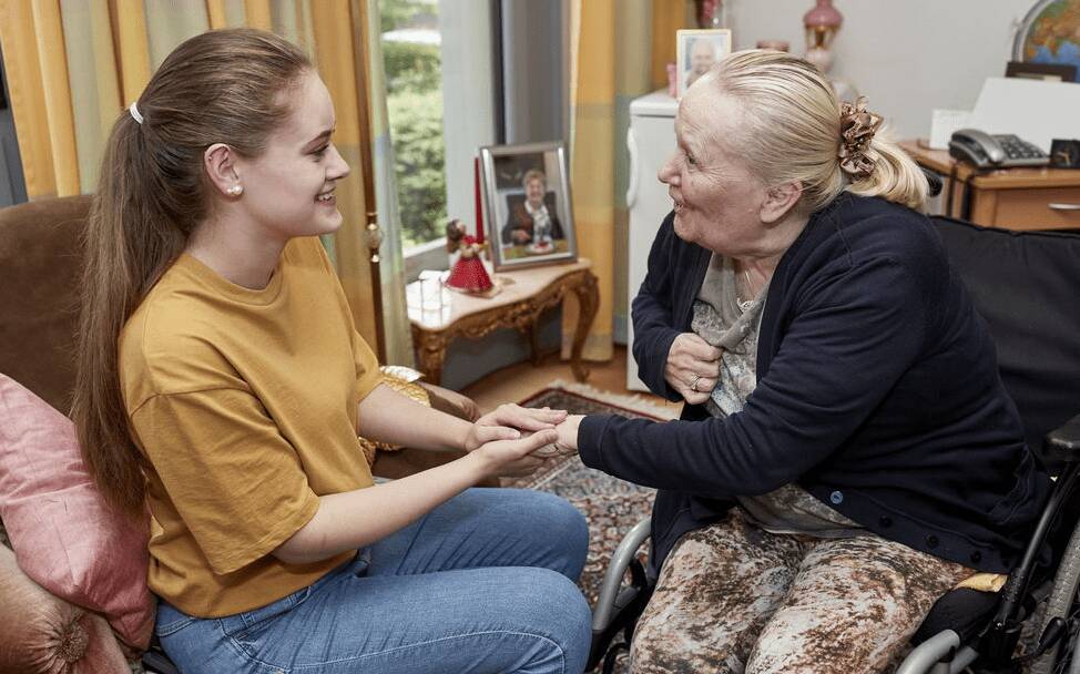 In einer Einzelbetreuungssituation nimmt eine junge Betreuungsmitarbeiterin während des Gesprächs die Hand der Bewohnerin.