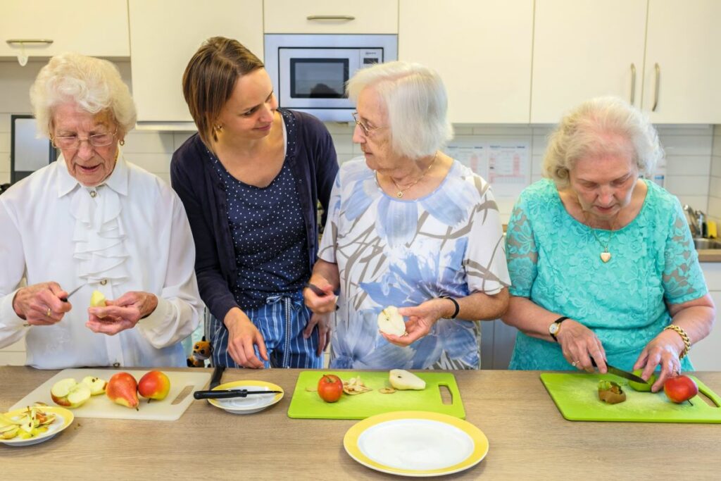 drei Heimbewohnerinnen kochen zusammen mit Heimmitarbeitering