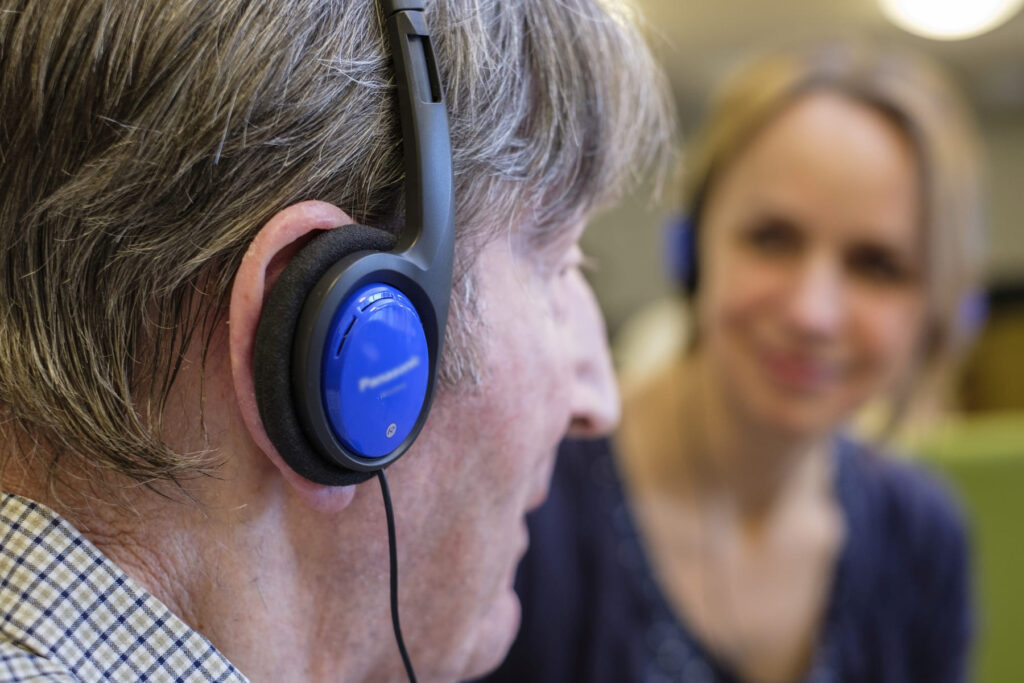Ein Mensch hört Musik über Kopfhörer und wird von einer Pflegekraft beobachtet