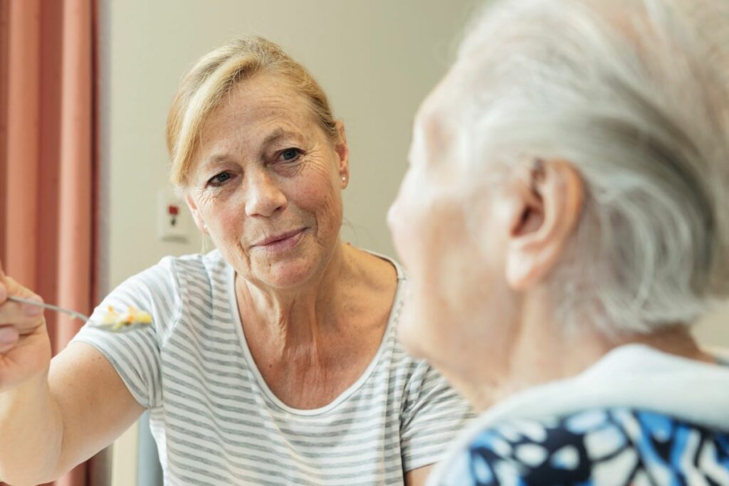 Heimmitarbeiterin füttert ältere Dame