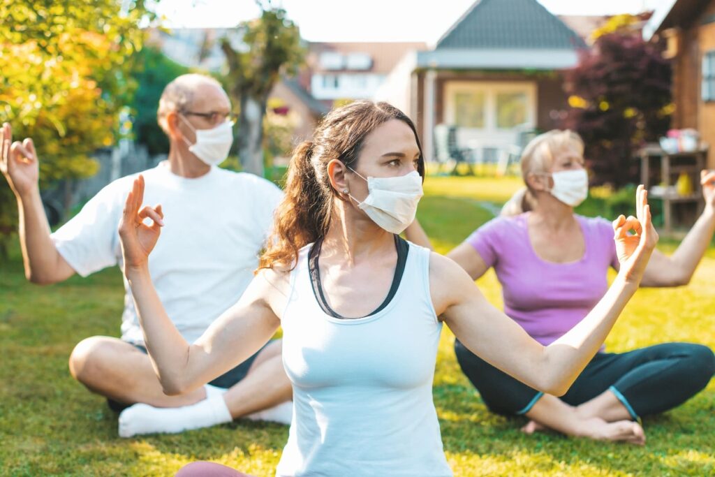 Drei Menschen im Schneidersitz praktizieren Yoga auf einer Wiese