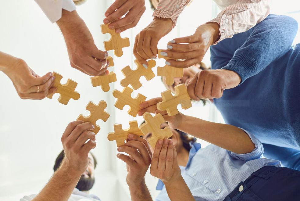 viele Hände in einem Kreis halten unterschiedliche Puzzle Teile aneinander