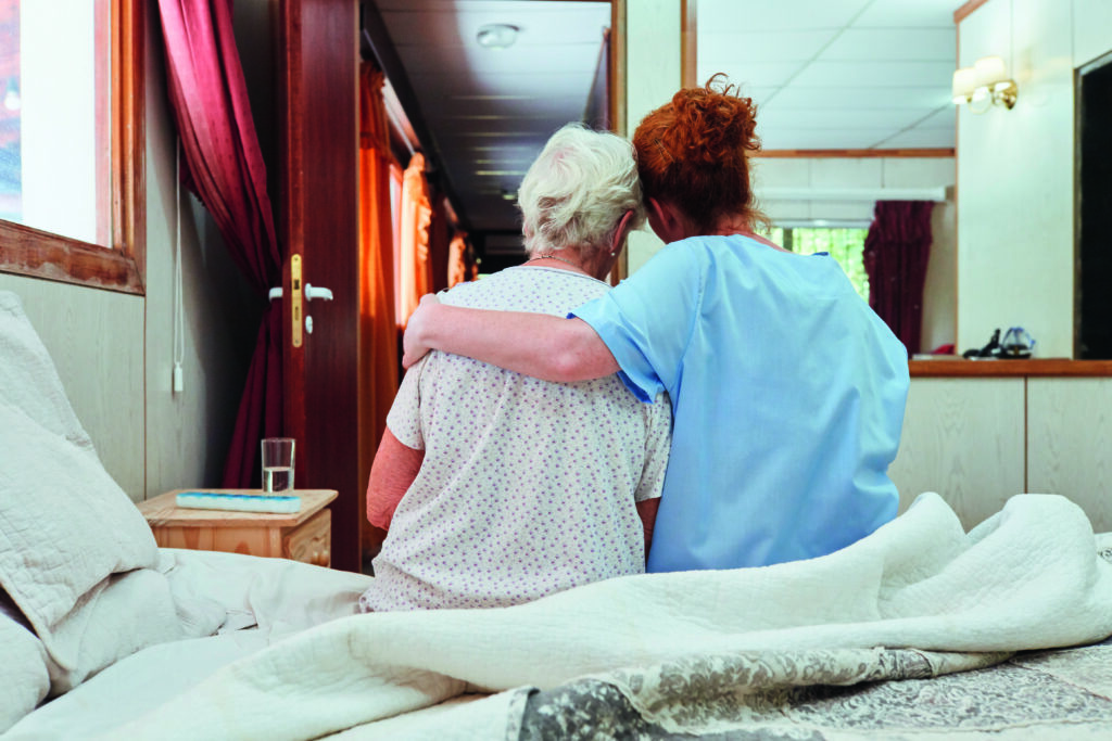 Krankenpflegerin umarmt Seniorin in Hospiz zum Trösten