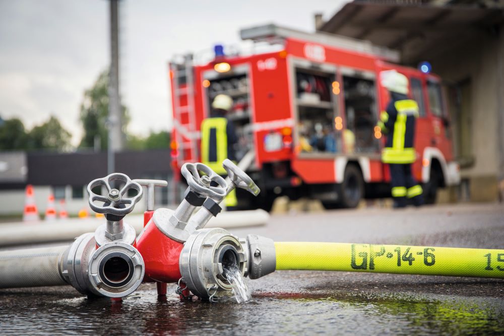 Feuerwehr und Rettungsdienst im Einsatz. Im Vordergrund liegt ein Feuerwehrschlauch.
