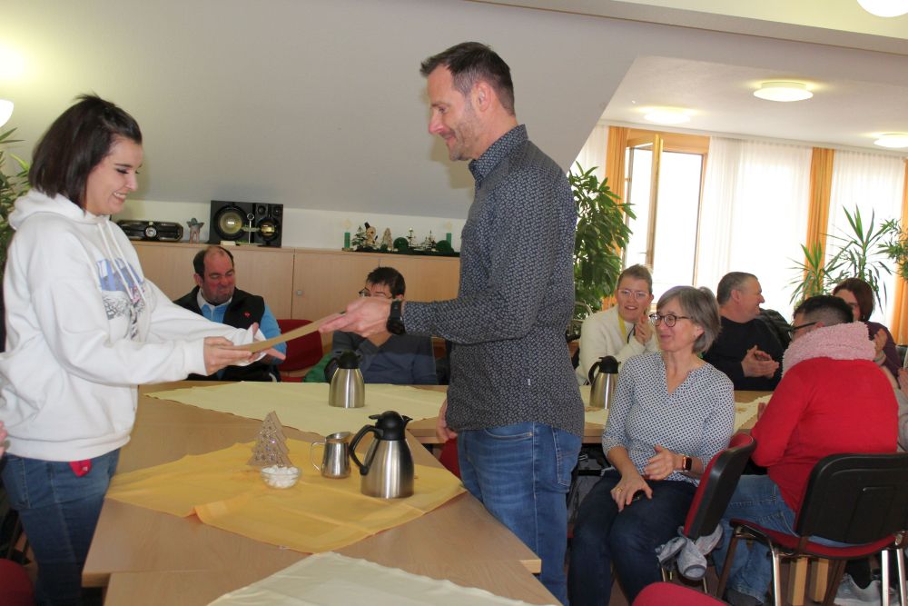 Martin Lutz (rechts), Arbeitsbereichsleitung Allgäu, überreicht Kübra Duman zum Abschied aus der Werkstatt für behinderte Menschen die Urkunde für zehn Jahre Mitarbeit.