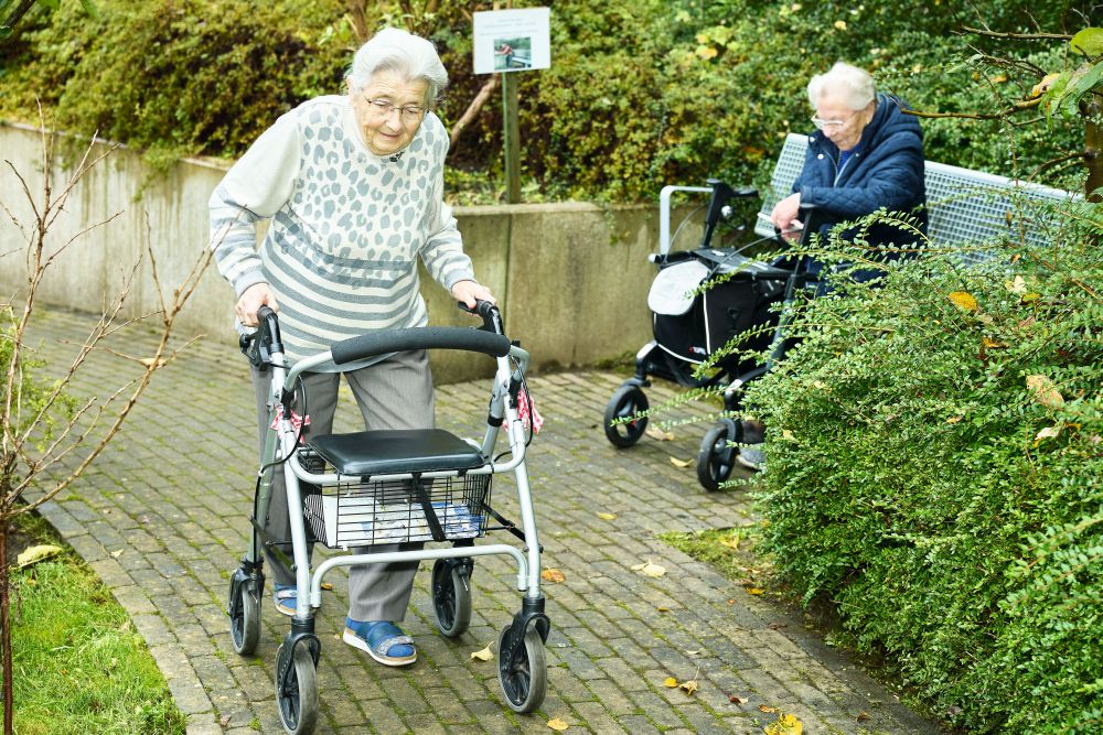 Ein ältere Frau läuft mit einem Rollator über einen Gehweg