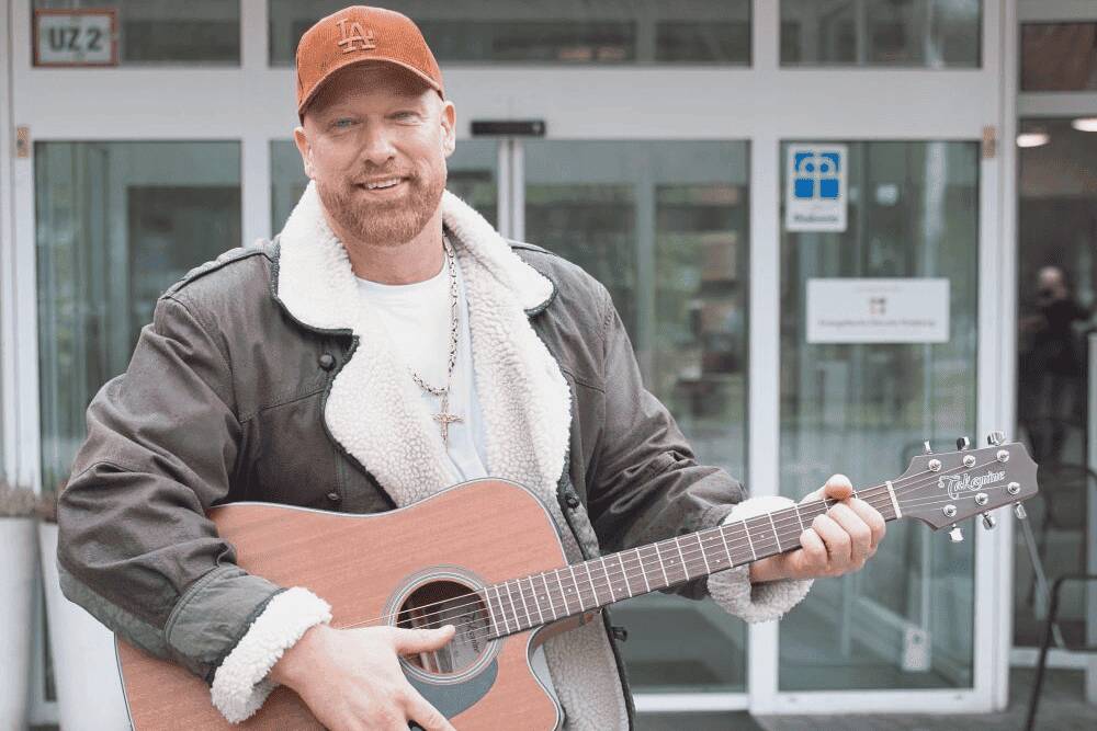 Adrian Armin Barein steht mit einer Gitarre vor dem Jochen Klepper Haus der Evangelischen Dienste Duisburg.