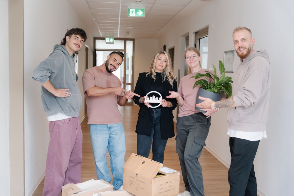 Junge Menschen stehen mit Umzugskarton in einem Flur.