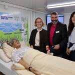 Jasmin Modis und Thorsten Hitzel (Martin Luther Stiftung Hanau) sowie Salomé Eggler (Google) im Mobilen Skills Lab (v.l.n.r.). Im Vordergrund ist die Pflege-Simulationspuppe zu sehen.
