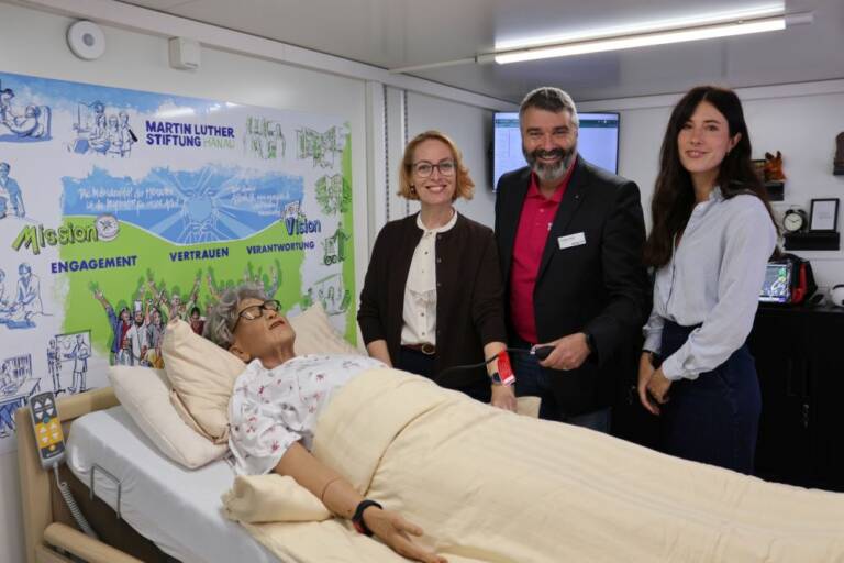 Jasmin Modis und Thorsten Hitzel (Martin Luther Stiftung Hanau) sowie Salomé Eggler (Google) im Mobilen Skills Lab (v.l.n.r.). Im Vordergrund ist die Pflege-Simulationspuppe zu sehen.